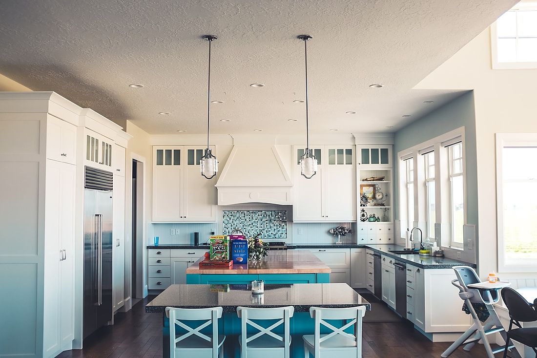 White kitchen with a blue-green island, bar chairs and glass pendant lights