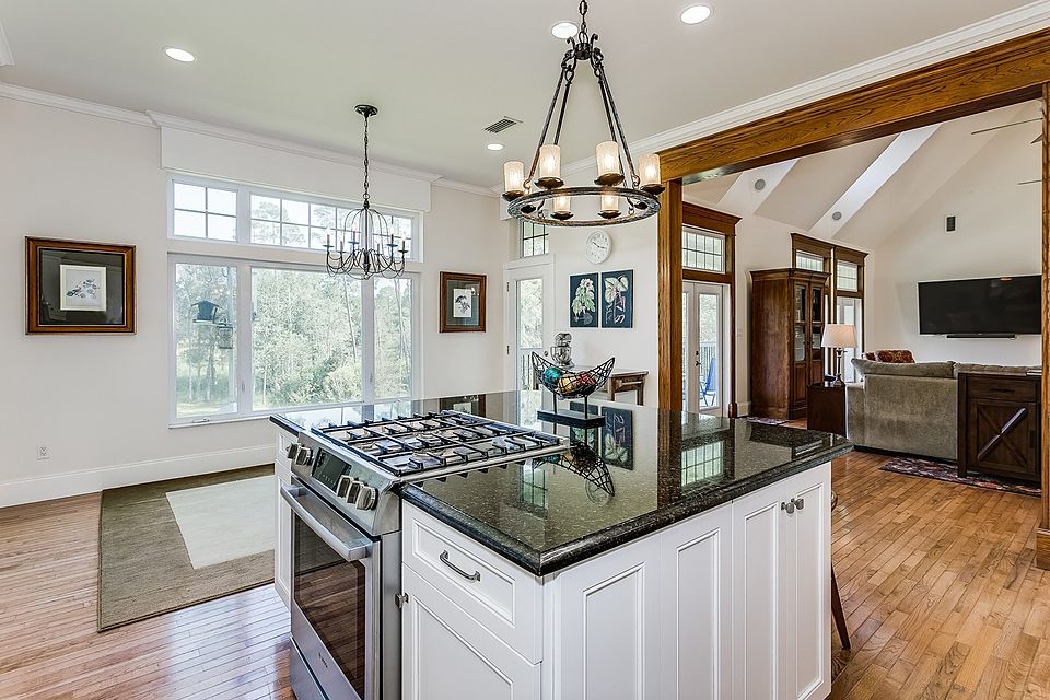 White island kitchen with a black granite top and an iron chandelier, open to a family room
