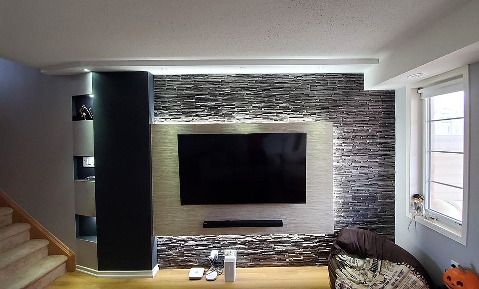 Finished basement family room with a stacked-stone media wall and a mounted TV