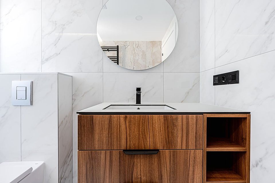 Modern bathroom with a walnut vanity, round mirror and white marble-look tile