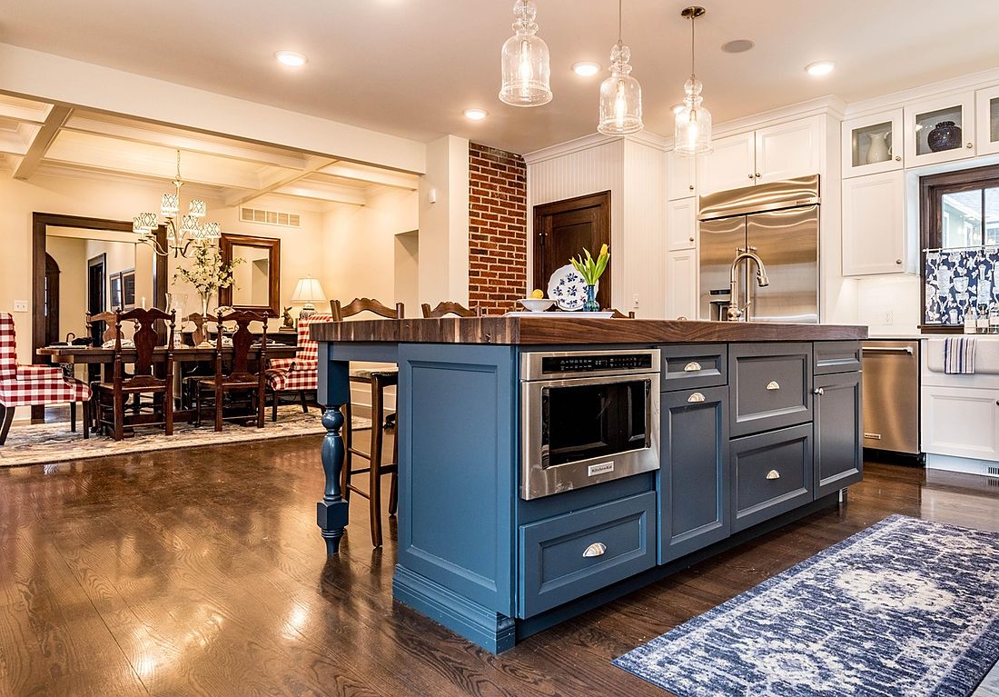 Open kitchen with a navy-blue island, butcher-block top, stainless appliances and glass pendant lights