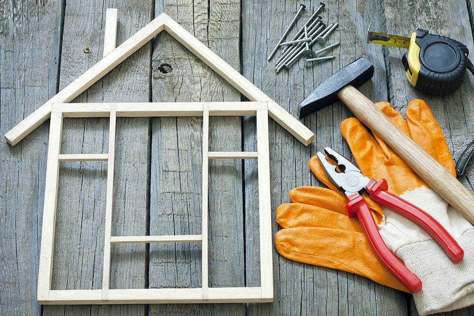 Small wooden house-frame model with a hammer, pliers, nails, tape measure and work gloves
