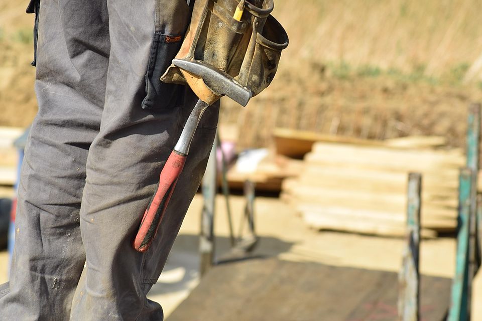 Carpenter's tool belt and hammer on a job site with stacked lumber, face not shown